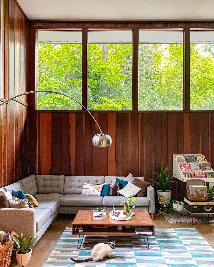 Mid-Century Modern living room with wood-paneled walls and windows on the perimeter of the room. Photo by instagram user @tinymightymidmod