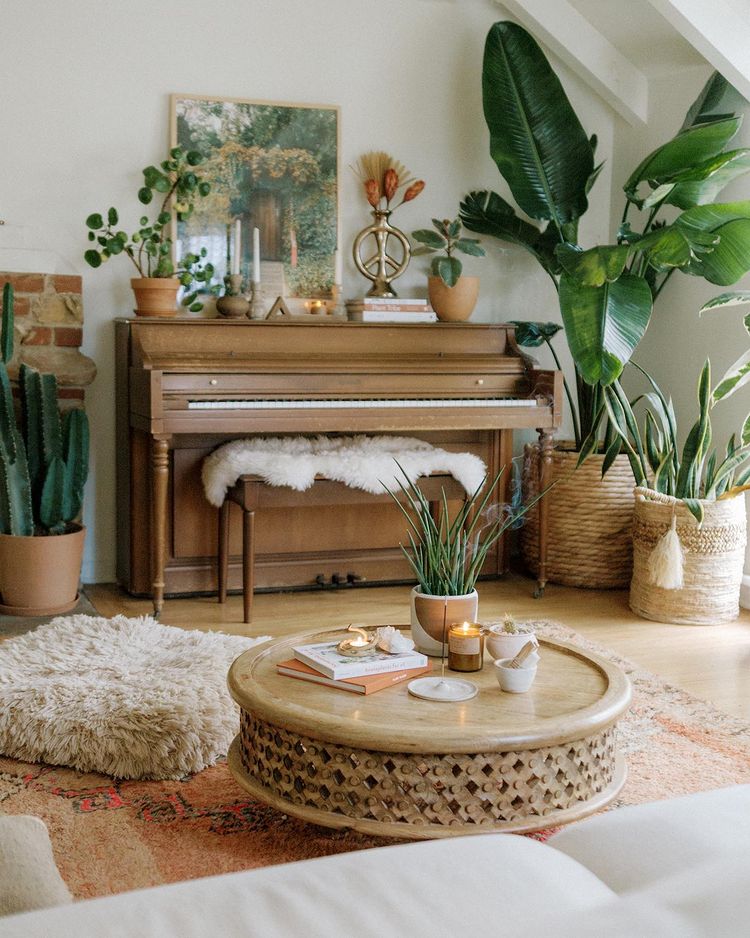 Urban jungle living area with soft pillows and a piano with large plants. Photo by instagram user @saratoufali