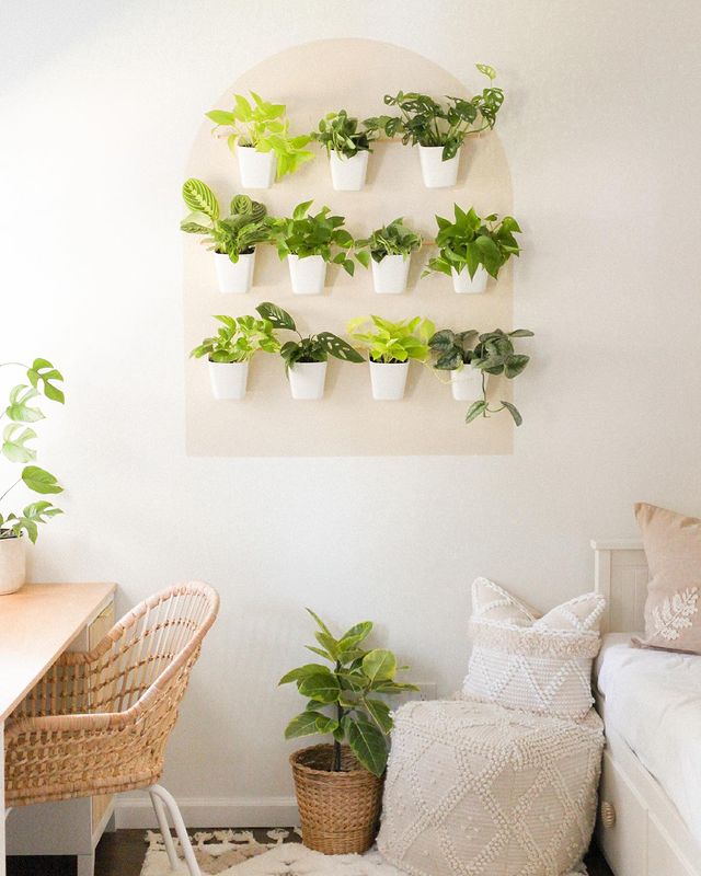 Modern jungle office with plants on the ground and desk and hanging from an organized plant wall hanger with multiple small white pots. Photo by instagram user @knots.and.pots.home