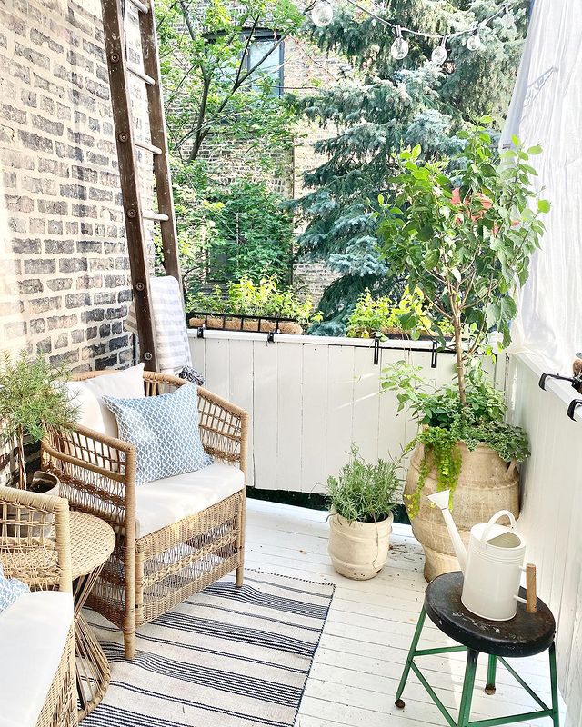 Modern apartment balcony with wicker chairs, area rug, and outside plants