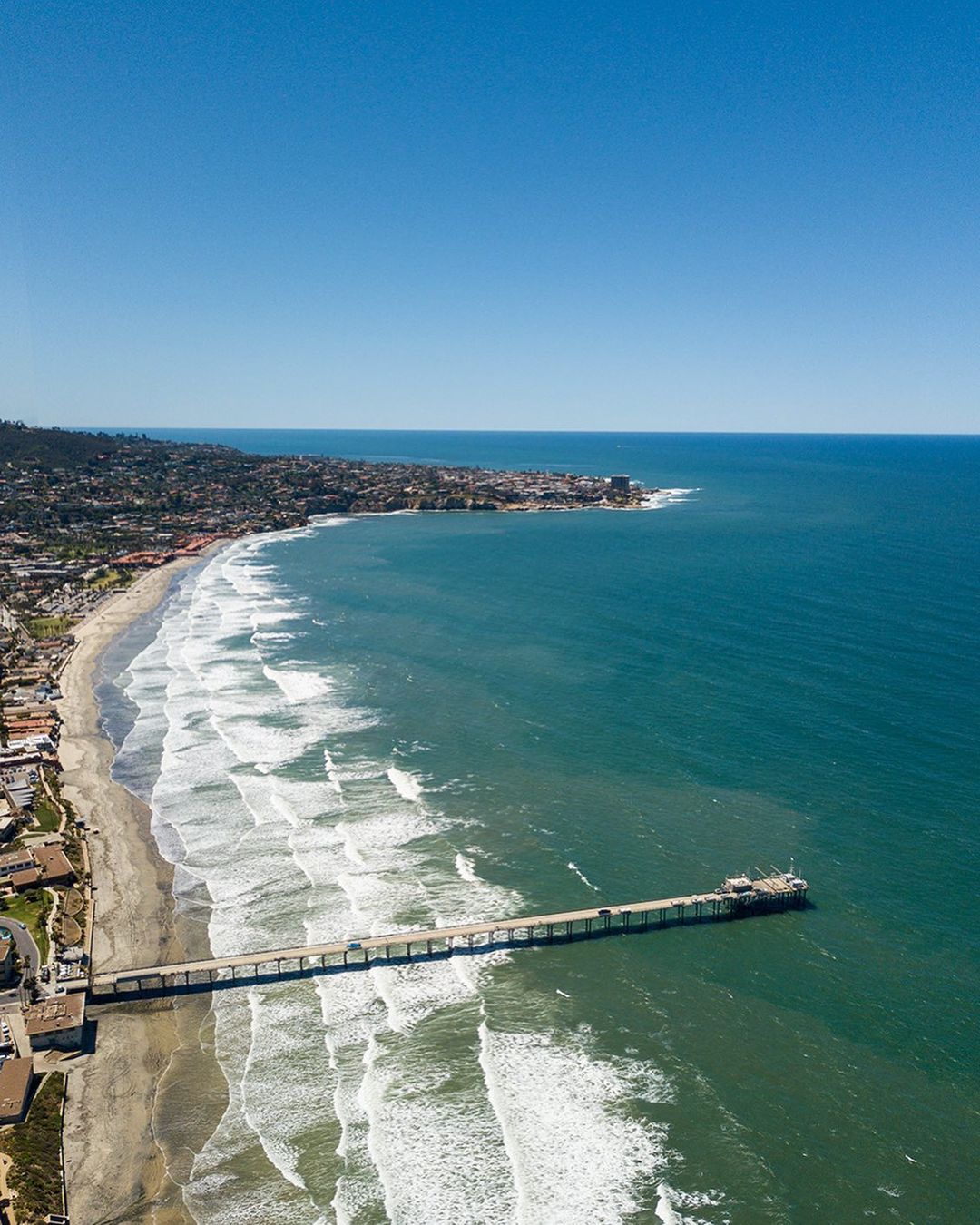 Landscape photo of a San Diego beach during a clear day with green and blue water. Photo by instagram user @bestudios_sd