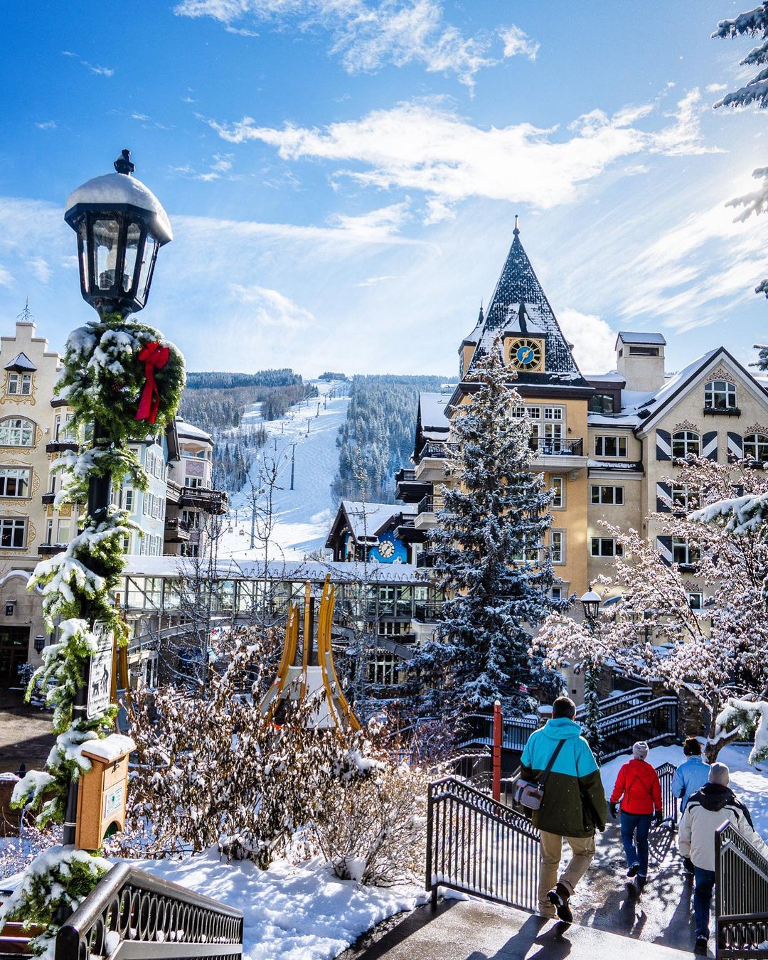 Downtown vail in the wintertime with holiday season decor and a ski slope with snowy roofs and people walking. Photo by instagram user @beyondtheblueridge