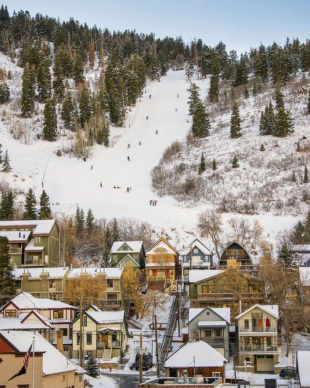 A quaint picture of Park City in the winter with houses covered in snow and people skiing on the mountainside. Photo by instagram user @visitparkcity