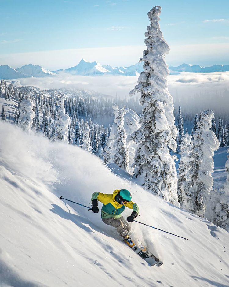 A bright action shot of intense skiing down a steep mountain hill with snow covered trees and a scenic background of Whitefish, Montana. Photo by instagram user @skiwhitefish