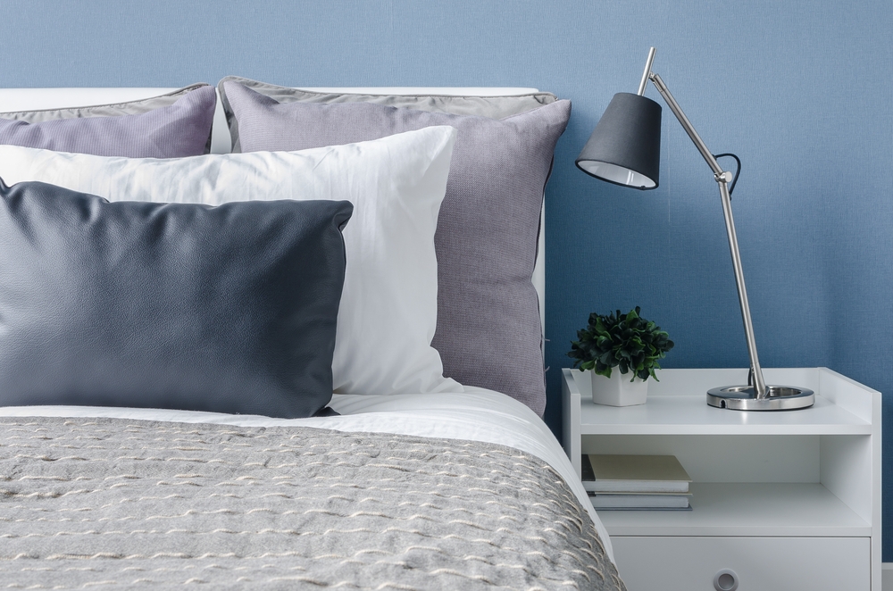 Close up of bedroom furniture featuring a bed, cool colored pillows, a nightstand, and metal lamp