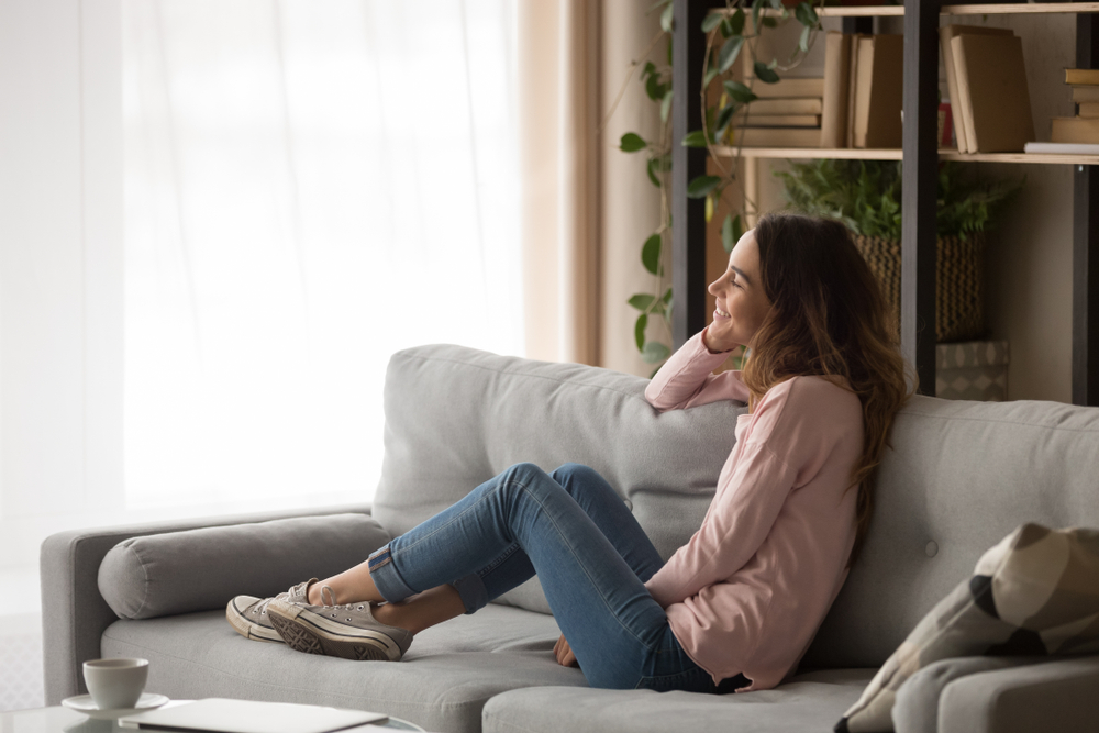 Smiling girl sitting on a comfortable couch in an apartment and looking out the window while smiling