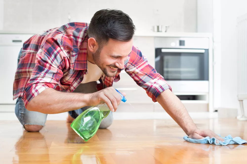 Smiling man cleaning hardwood floors in a kitchen