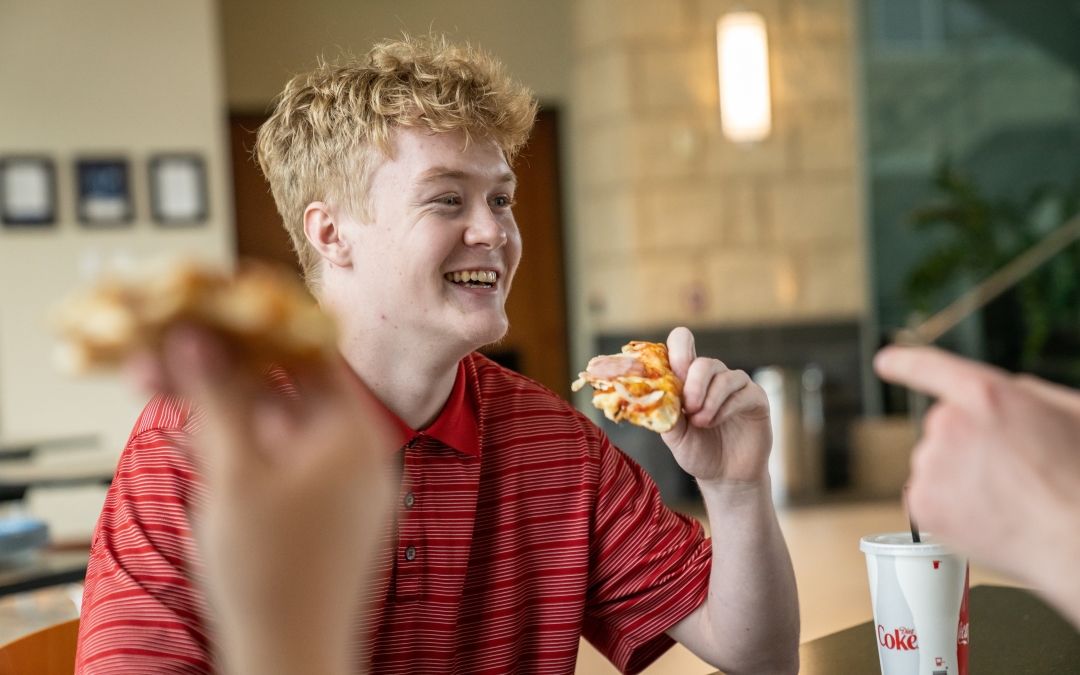 Man Sitting and Laughing While Eating Pizza