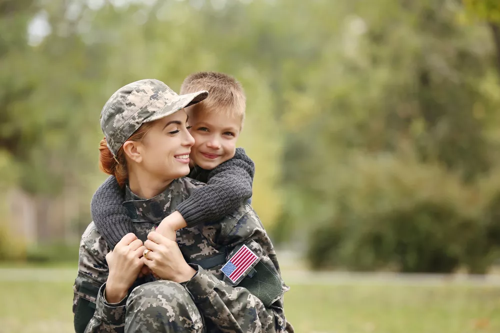 Military mother giving her child a piggy-back ride on her shoulders in a meadow.