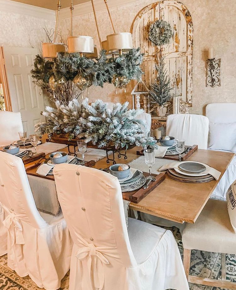 A wooden christmas talbe with pine features and chairs surrounding it with slipcovers. Photo by instagram user @savvyinthesuburbs
