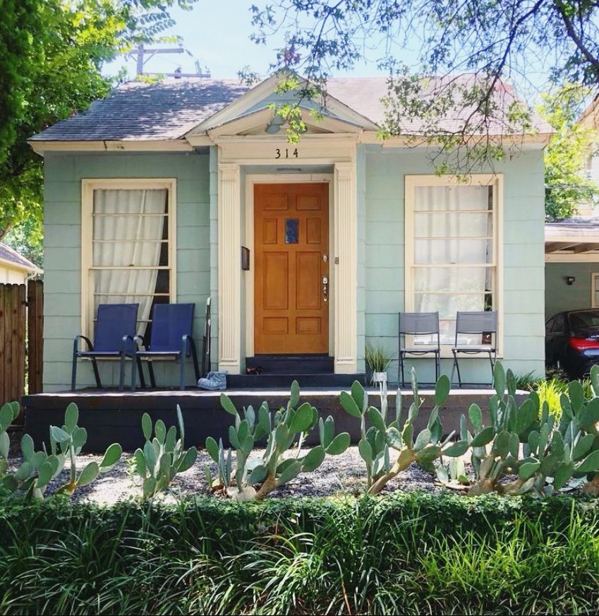Exterior shot of a blue home with a wooden door for rent in Oak Cliff. Photo from Instagram user @proxyproperty
