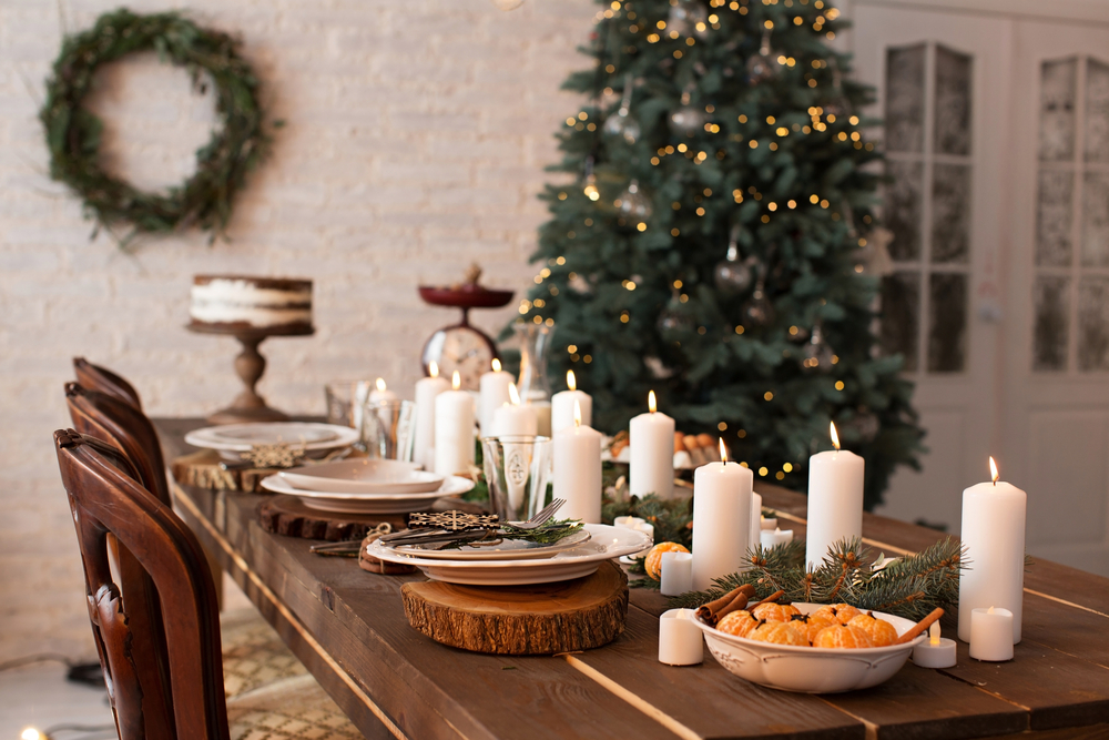 Rustic Christmas table with white candles and wooden place settings and a large christmas tree with white lights in the background.
