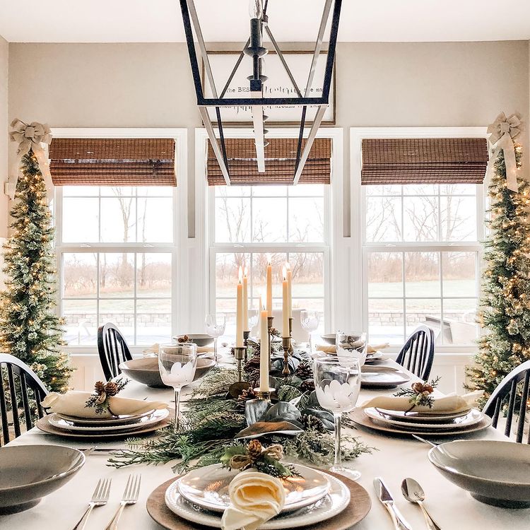 Christmas table with a lot of natural light and garland with a white tablecloth and beautiful place settings. Photo by instagram user @homeonnativetrail