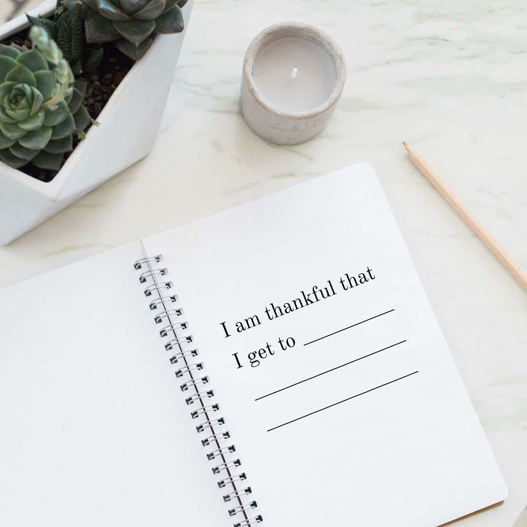 Gratitude journal saying "I am thankful that I get to" on desk with pencil, candle, and box of succulents | Photo bye Instagram user @mytrainerjill