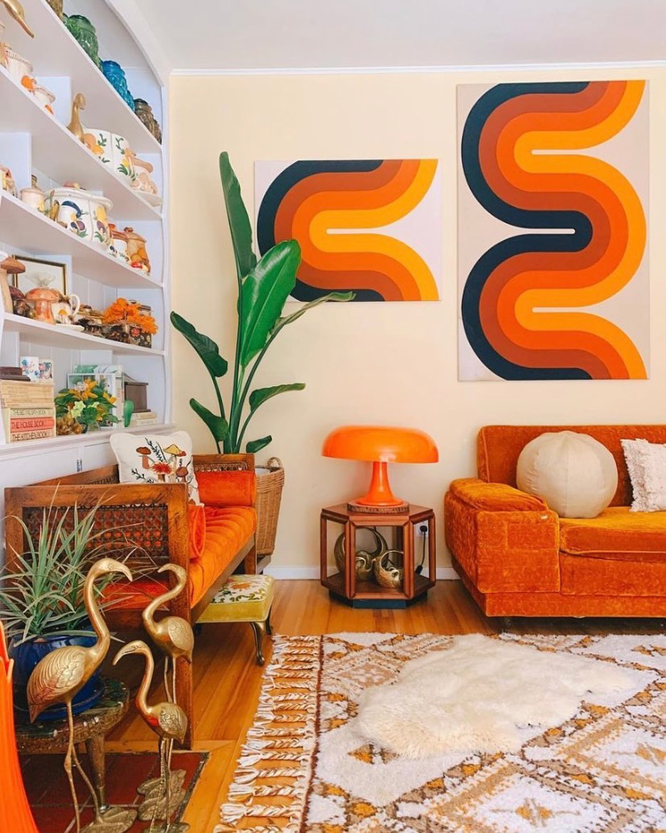 Interior shot of boho living room with orange couch, golden flamingo figurines, and bold artwork | Photo by Instagram user @chanel.lauren.roth
