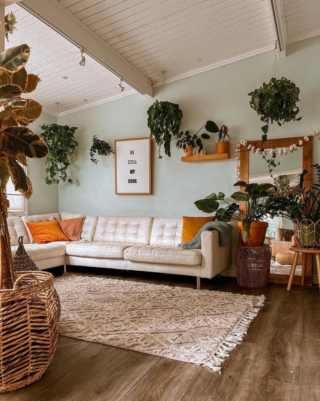 Interior shot of bohemian living room with white couch, white rug, orange accent pillows, and many houseplants | Photo by Instagram user @shannieee