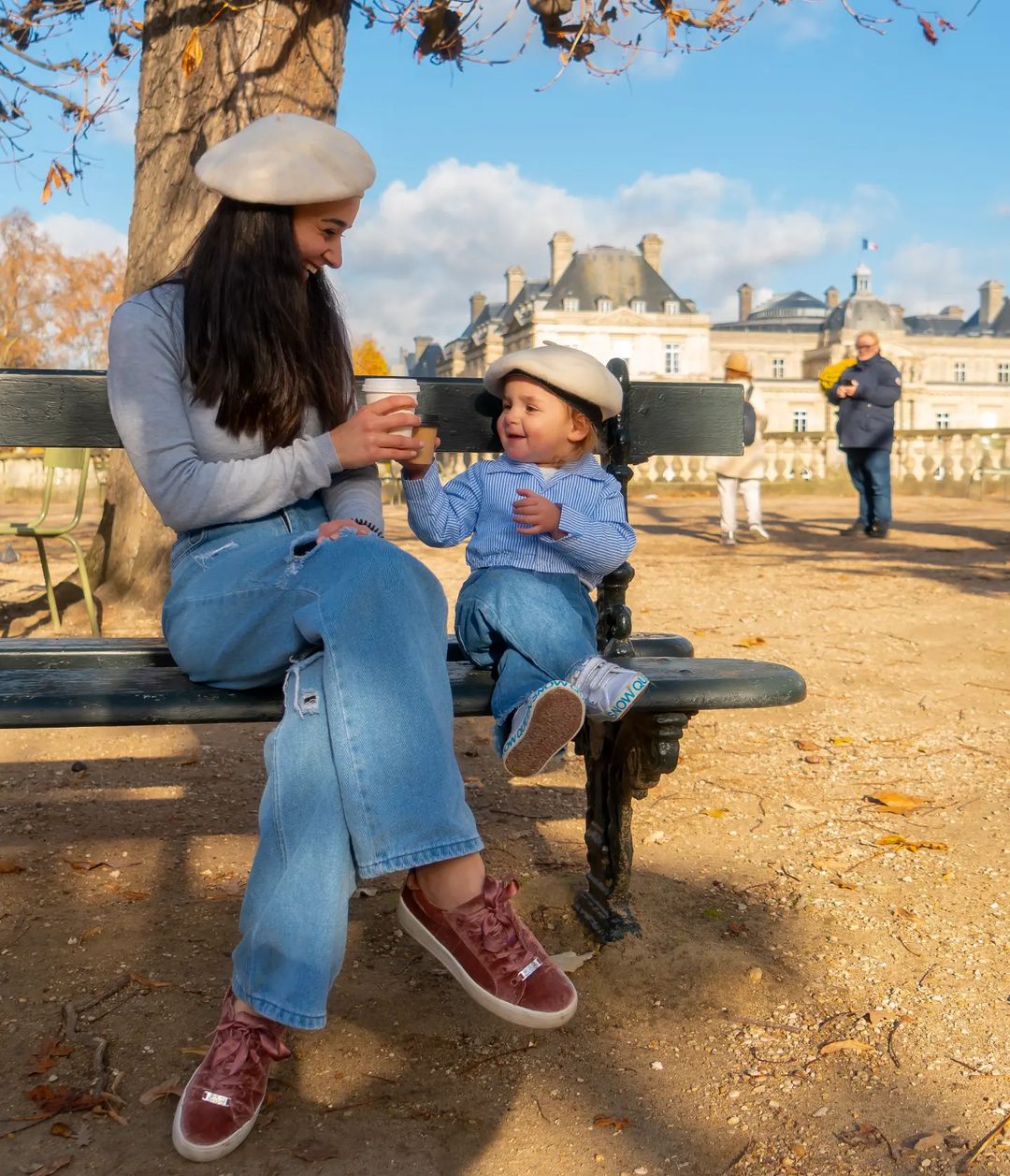 Mother and son wearing matching outfits with blue jeans, blue long-sleeve shirts, and white berets while in sitting on a park bench in Paris | Photo by Instagram user @rindalaakl