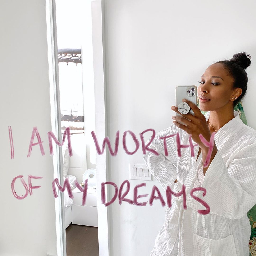 Bathroom selfie of woman in white robe with positive affirmation "I am worthy of my dreams" written in pink lipstick on the glass | Photo by Instagram user @sashaexeter