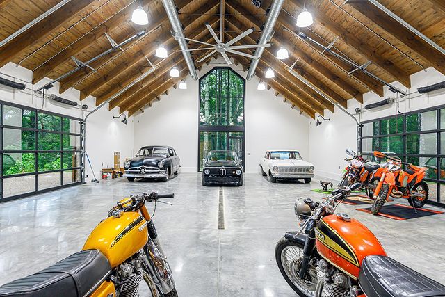 Large garage space with vaulted wooden beam ceiling, a large ceiling fan, and multiple luxury cars and motorcycles. Photo by Instagram user @livingstonedesignbuild