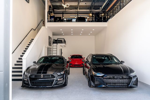 Interior of garage with multiple vehicles and stair leading up to a lofted lounge. Photo by Instagram user @thevaults