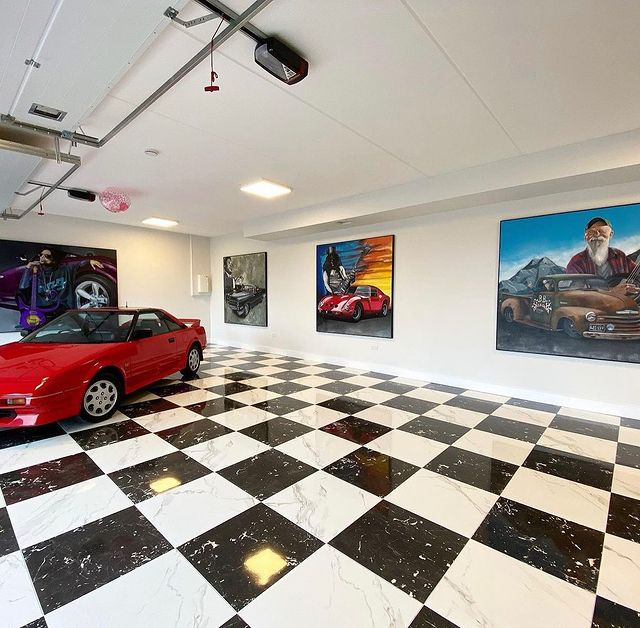Interior of a garage with black and white checkered tile floor, a few paintings hung on the back wall, and a red car in the corner. Photo by Instagram user @our_emeraldhome