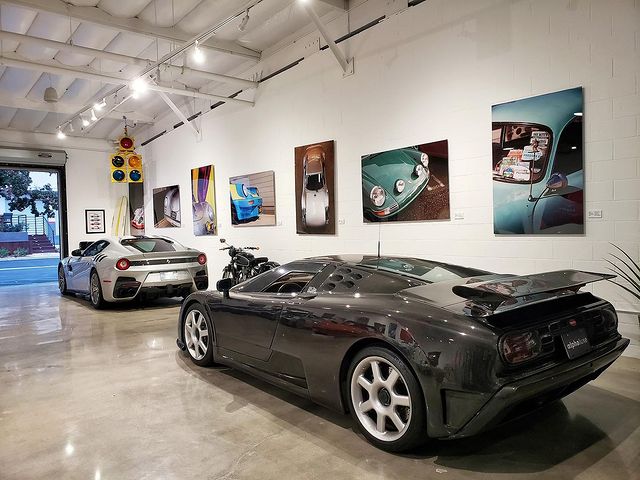 Interior of a garage with two luxury cars and many pieces of art hung on the wall. Photo by Instagram user @finishlineautoclub