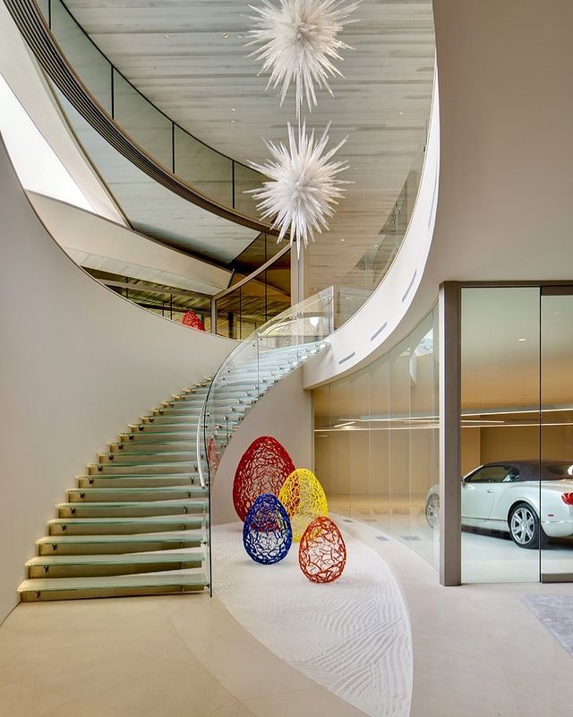 Interior of a luxury home with staircase leading to the second floor and a vehicle displayed behind glass on the first floor. Photo by Instagram user @hillconstructioncompany