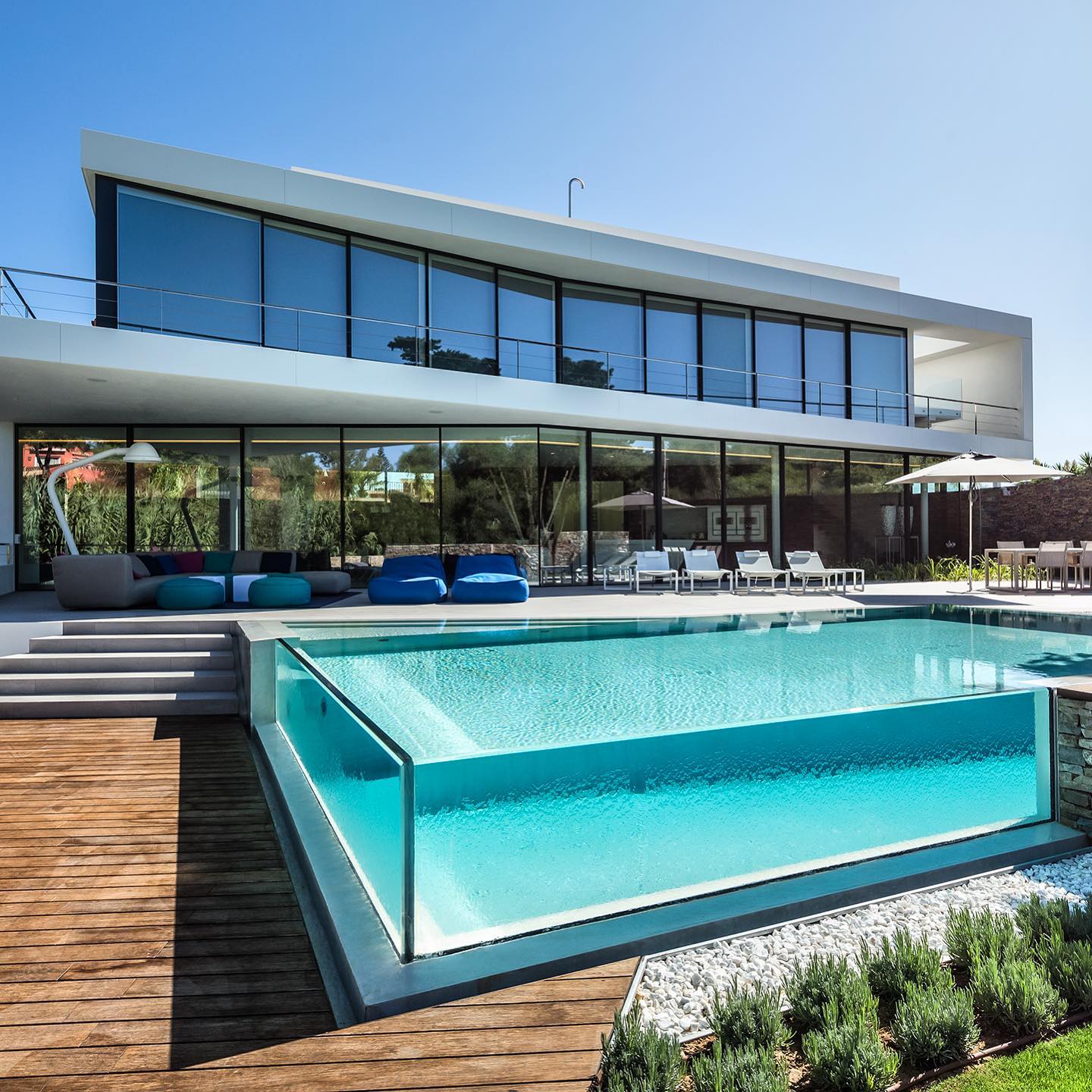 modern home with light blue pool with glass walls on the deck. Photo via Instagram user @iqglassinternational