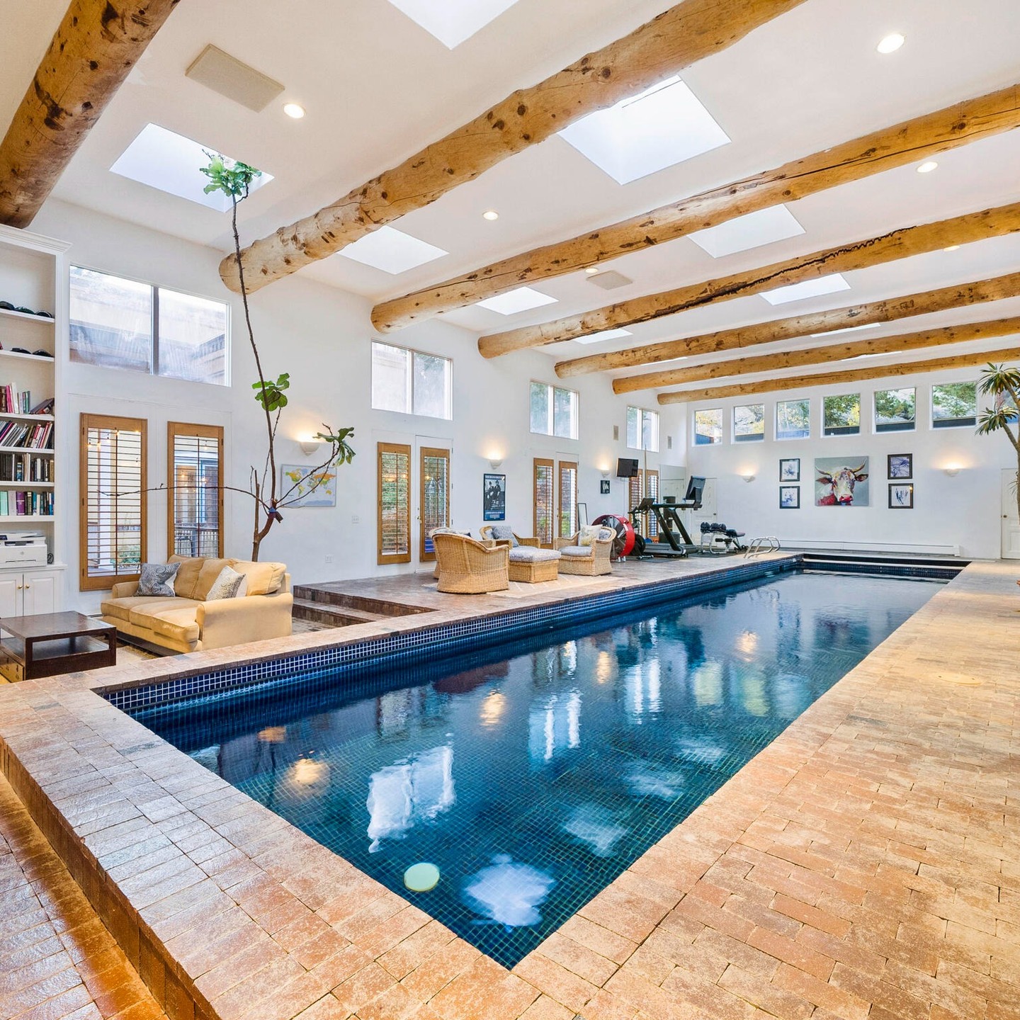 dark blue indoor swimming pool with natural wood beaming and lounge chairs. Photo via Instagram user @livsothebysrealty
