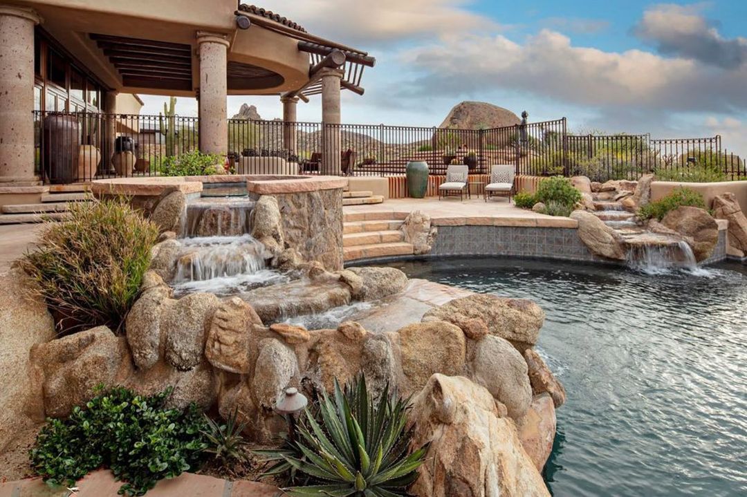 swimming pool with natural rock waterfall and landscaping. photo via Instagram user @realestate_magazine