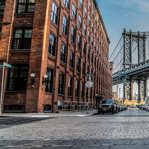 New York City brick street and brownstone building with Brooklyn Bridge in background