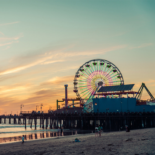 Lit up ferris wheel on Los Angeles beach boardwalk at sunset