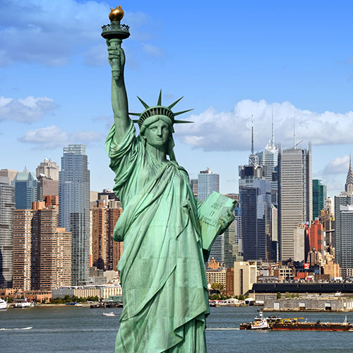 Statue of Liberty from waist up in front of New York Harbor and skyscrapers