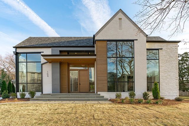 A modern home with huge glass windows, wooden panels, and white stone bricks stands on a sunny day in North Hills, Raleigh. Photo via Instagram user @homesteadbuilt