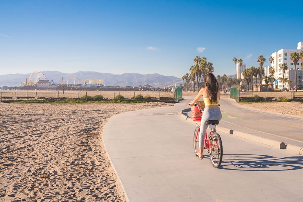 Woman riding bike on sunny Los Angeles beachfront sidewalk 