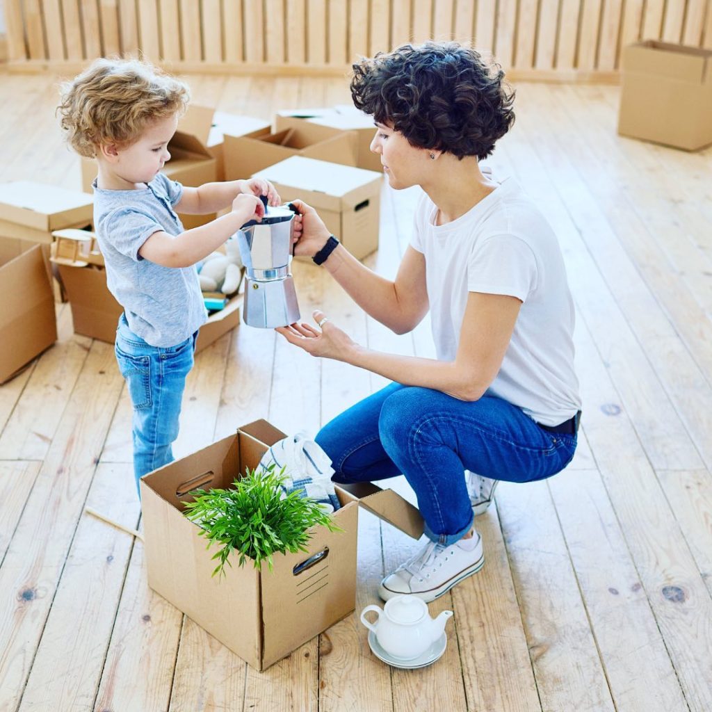 A young adult showing a child a coffee press surrounded by unpacked boxes. Photo via Instagram user @greatdaymoving