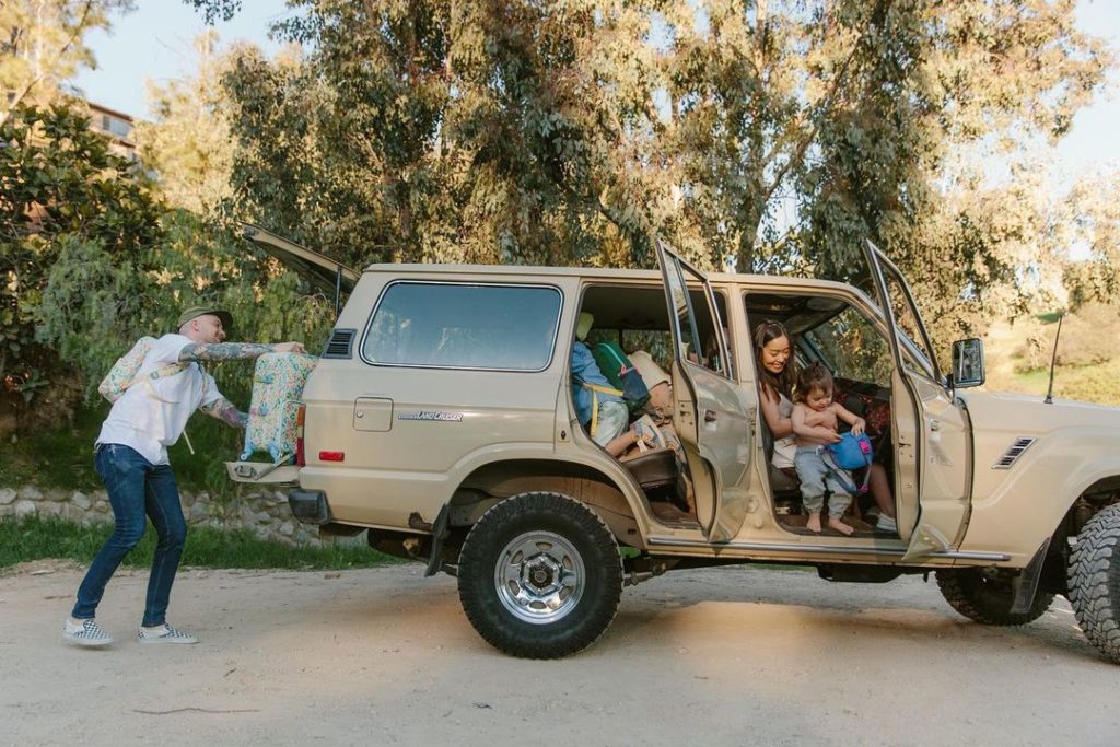 A family of four packing a jeep with bags while the doors and trunk are open in a forest. Photo via Instagram user @statebags