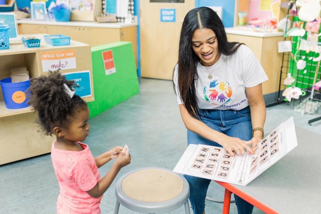 Young woman reading a picture book to a child in a childcare setting. Photo via Instagram user @ itsjustchillcounseling