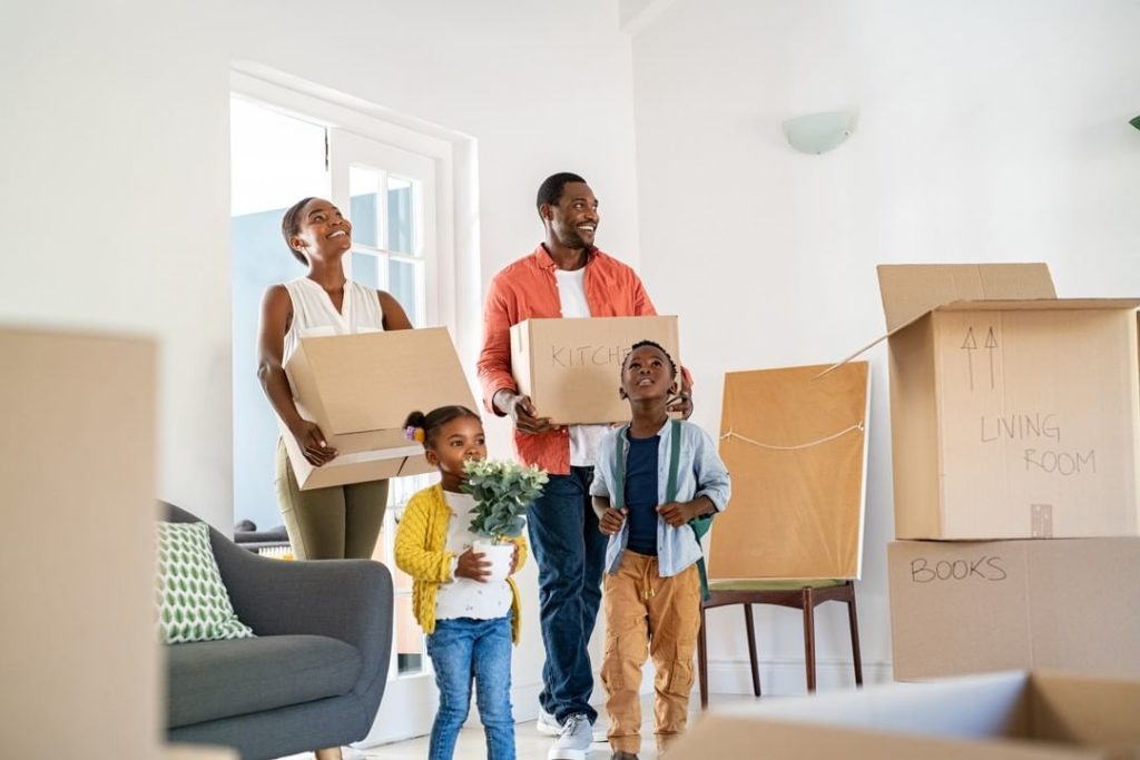 A family of four looking at their new home with wonder while holding moving boxes. Photo via Instagram user @dablnetwork