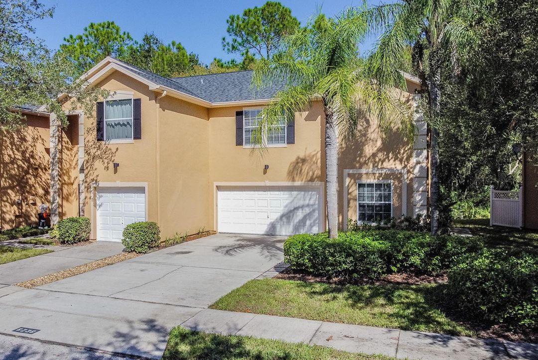 Tan stucco house with white garage doors and green trees. Photo by Instagram user @melissawolffe_tampahomes