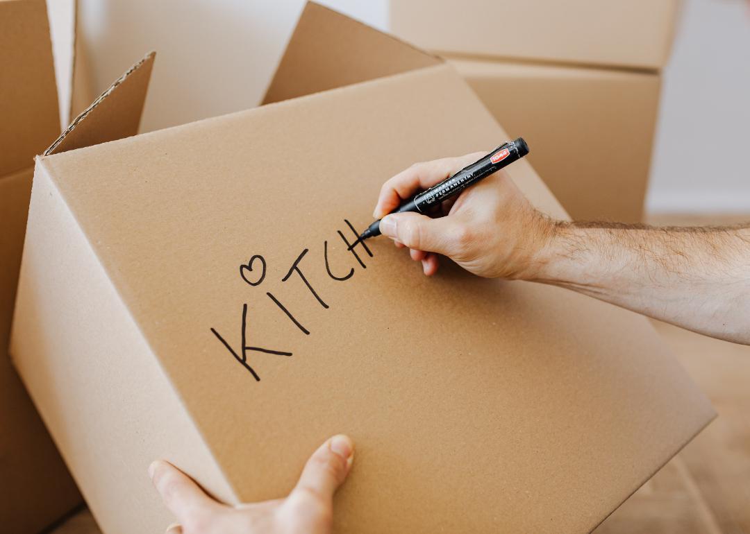 Person writing "Kitchen" on a moving box with permanent marker