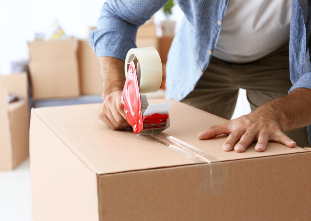 Young man's hands holding box while he uses packing tape