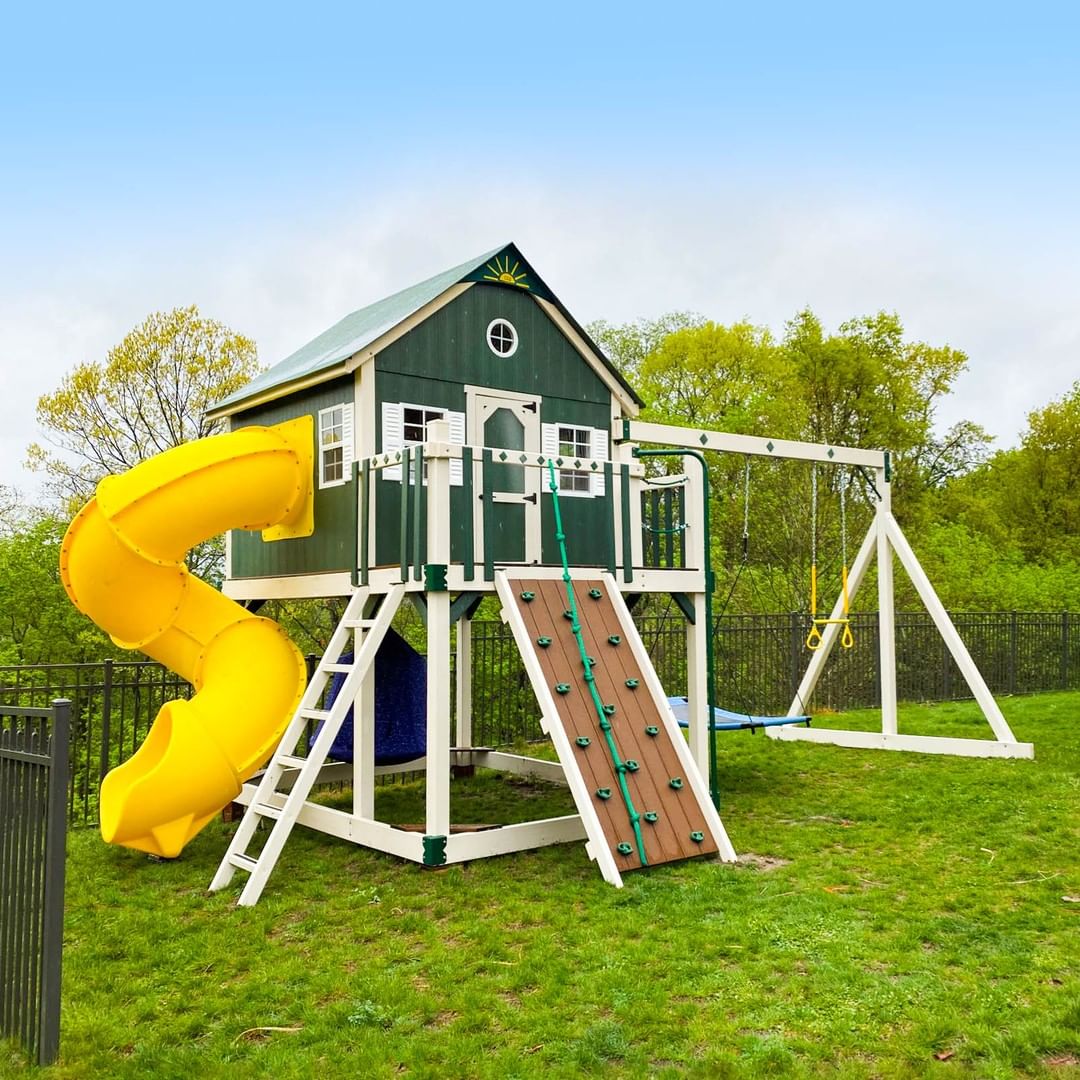Green playset with swings, rock climbing wall, and yellow slide. Photo by Instagram user @kingswingsplay