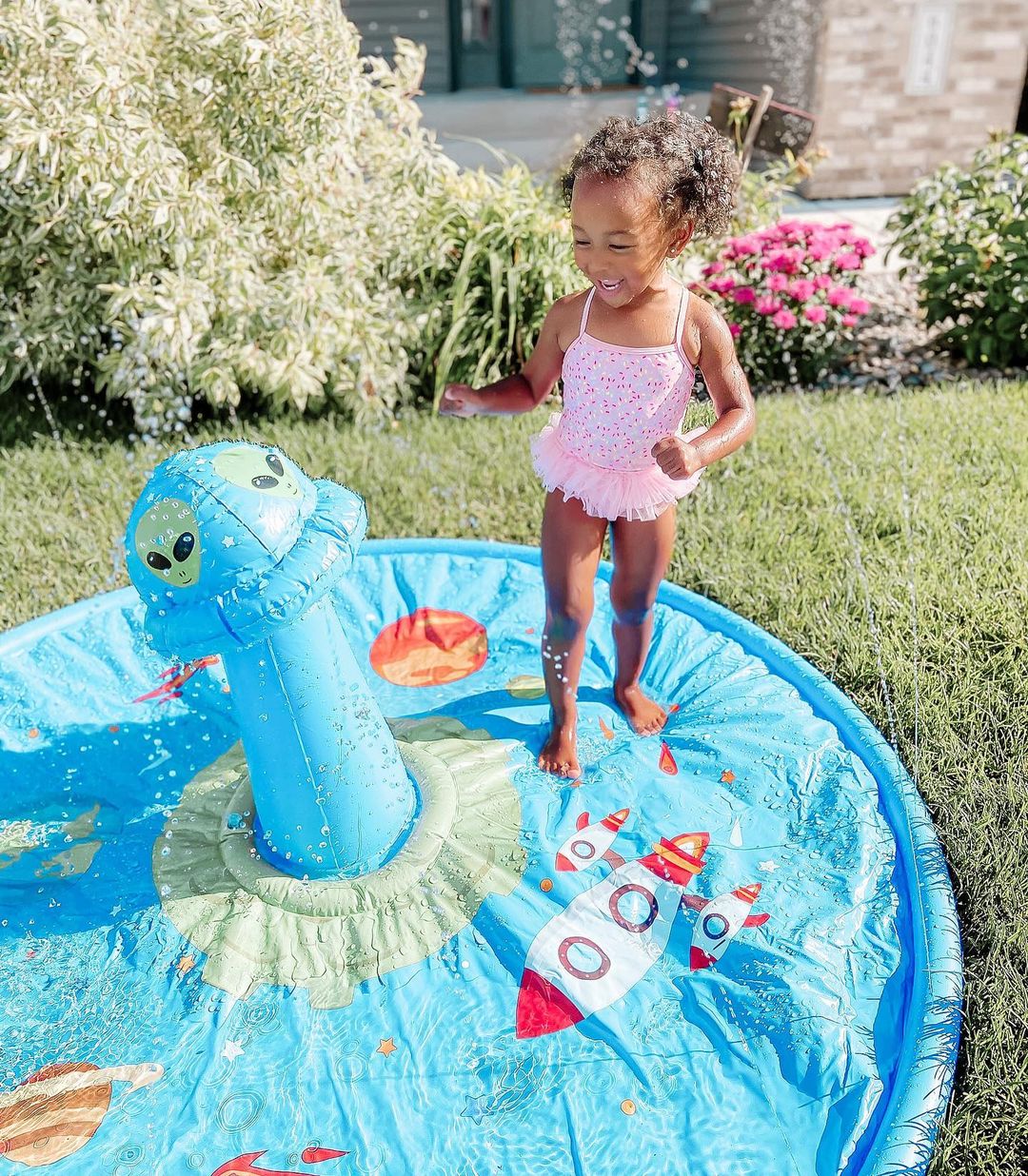 Child smiling using a backyard water splashpad. Photo by Instagram user @lienonme