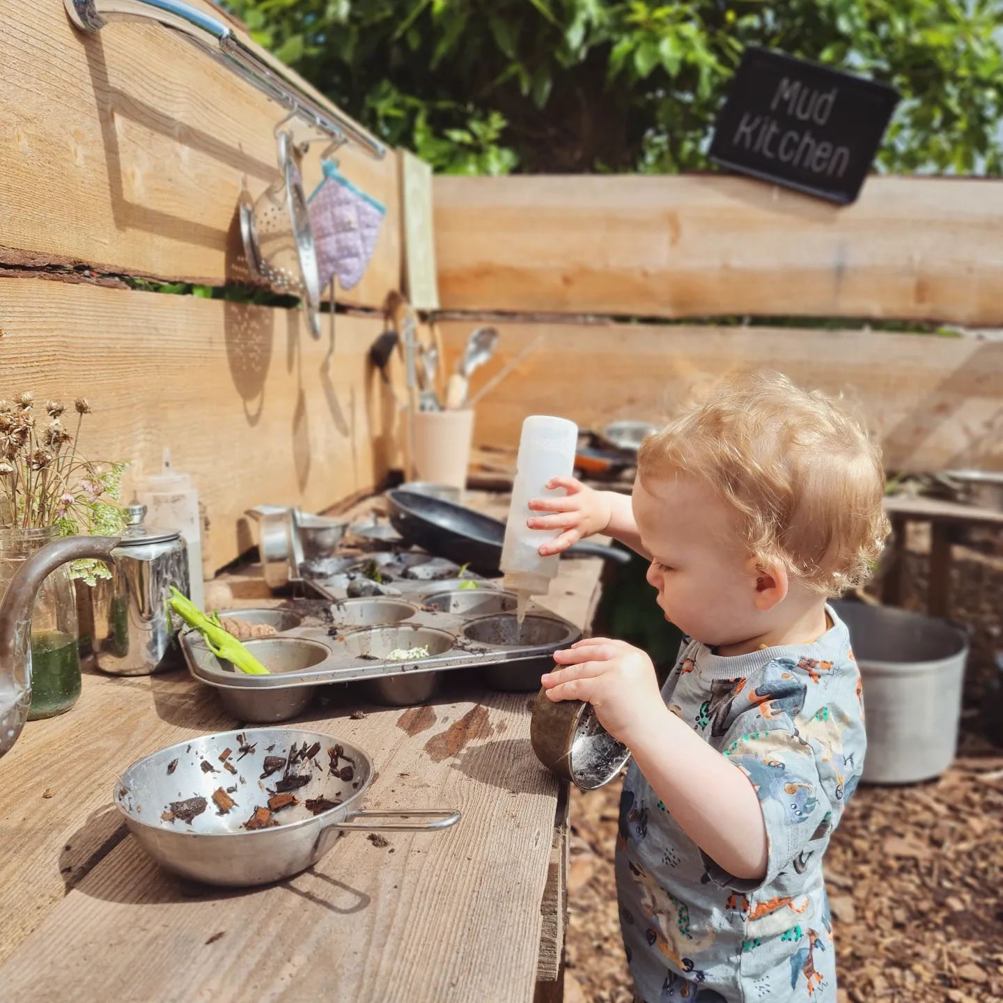 DIY mud kitchen with cake pans and cooking utensils. Photo by instagram user @wild_little_wonderers