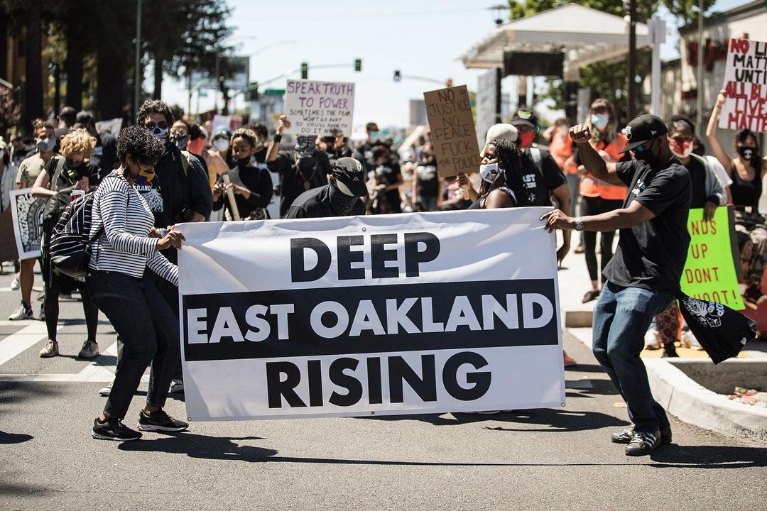Protesters holding the banner "Deep East Oakland Rising" on the streets. Photo by Instagram username @amirazizphotos