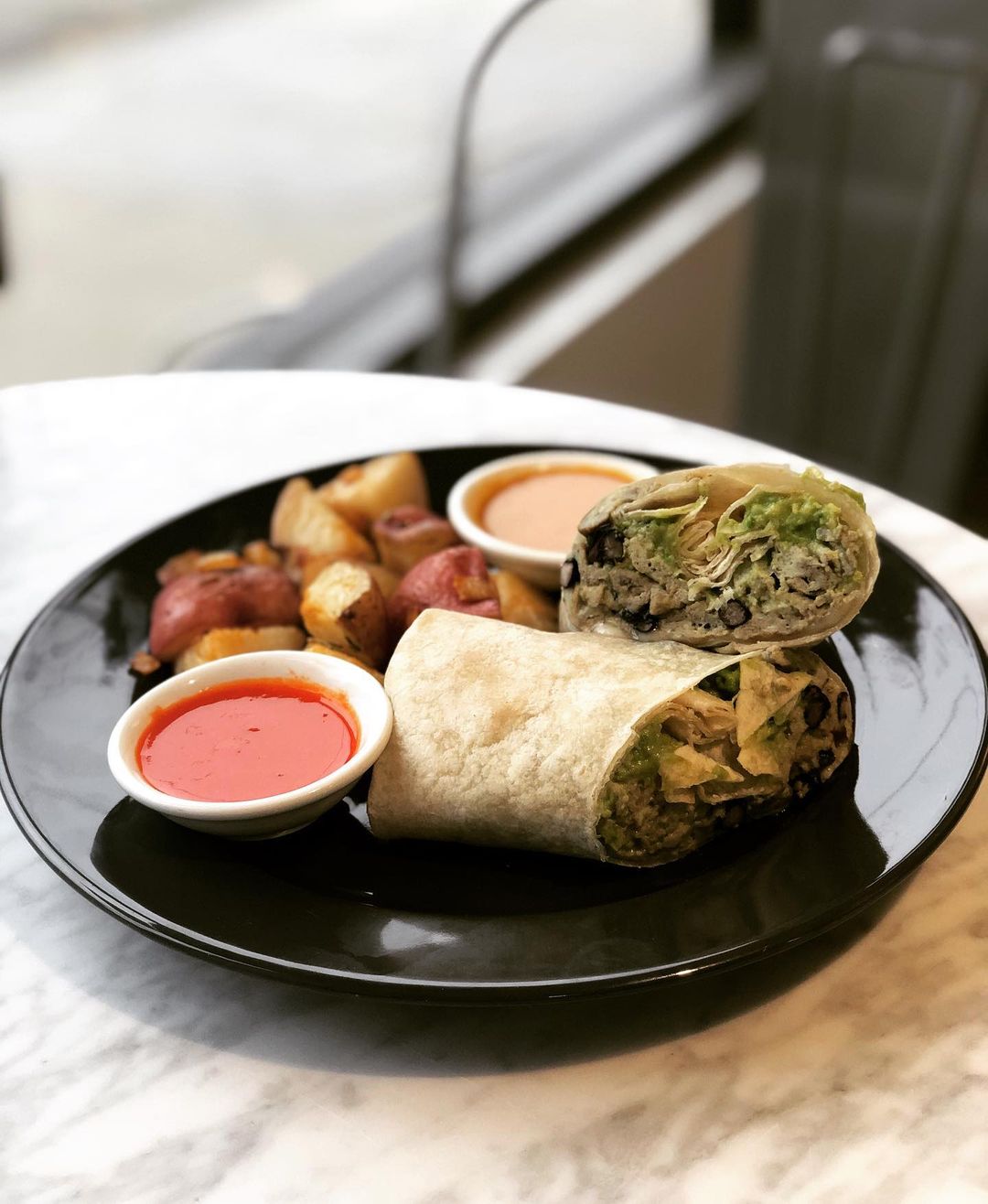 Breakfast wrap with rosemary roasted potatoes and fresno chili hot sauce on a plate. Photo by Instagram username @petitcafeoak
