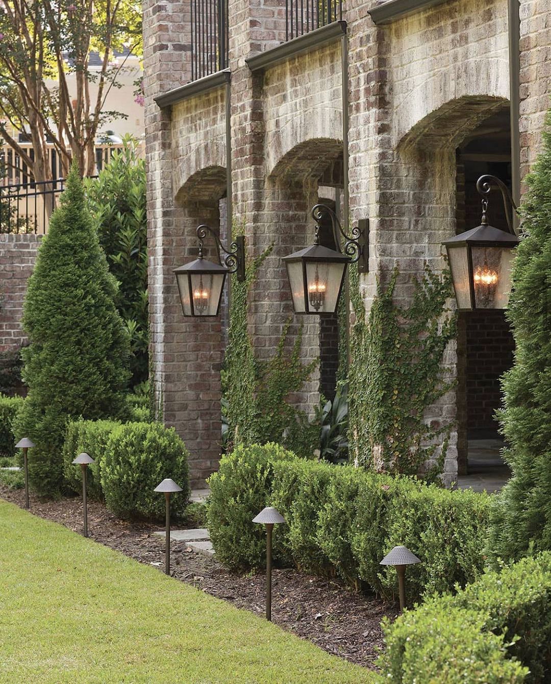 Large outdoor wall sconces on a brick home with green hedges. Photo by Instagram user @mylightingsource