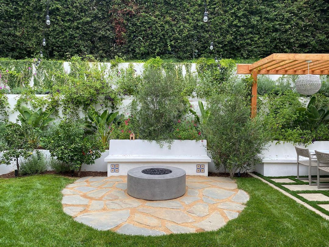 A backyard patio with built-in seating behind a fire pit. Photo by Instagram user @elowlandscape
