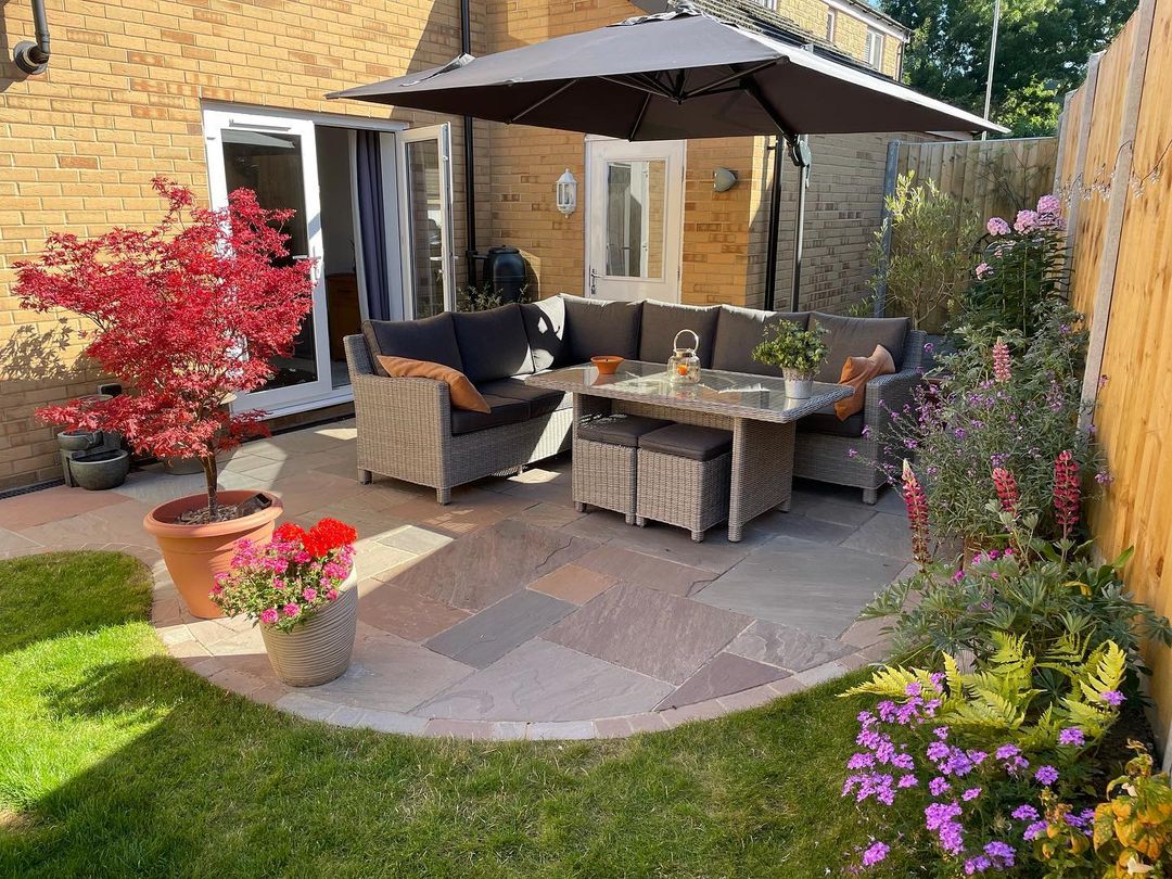 A backyard patio with stone pavers and a patio furniture set under an umbrella. Photo by Instagram user @paulholbrookpaving